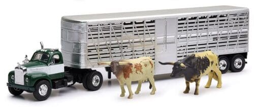 A toy cow standing next to a truck.