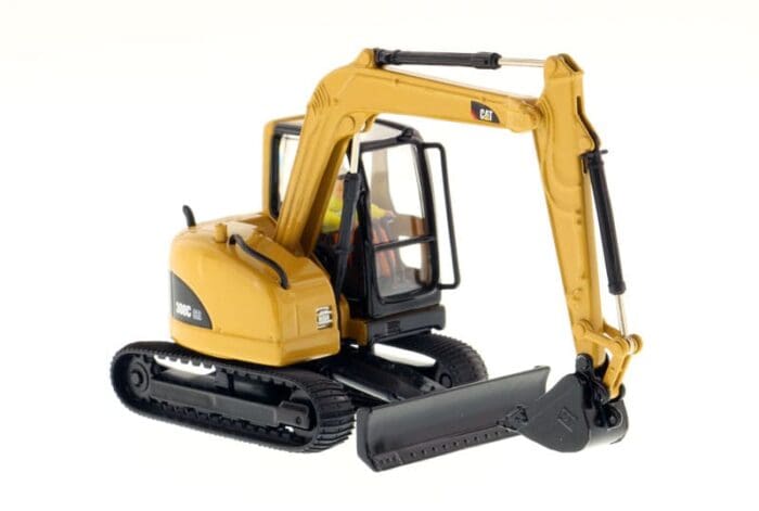 A yellow and black toy excavator is next to a white wall.